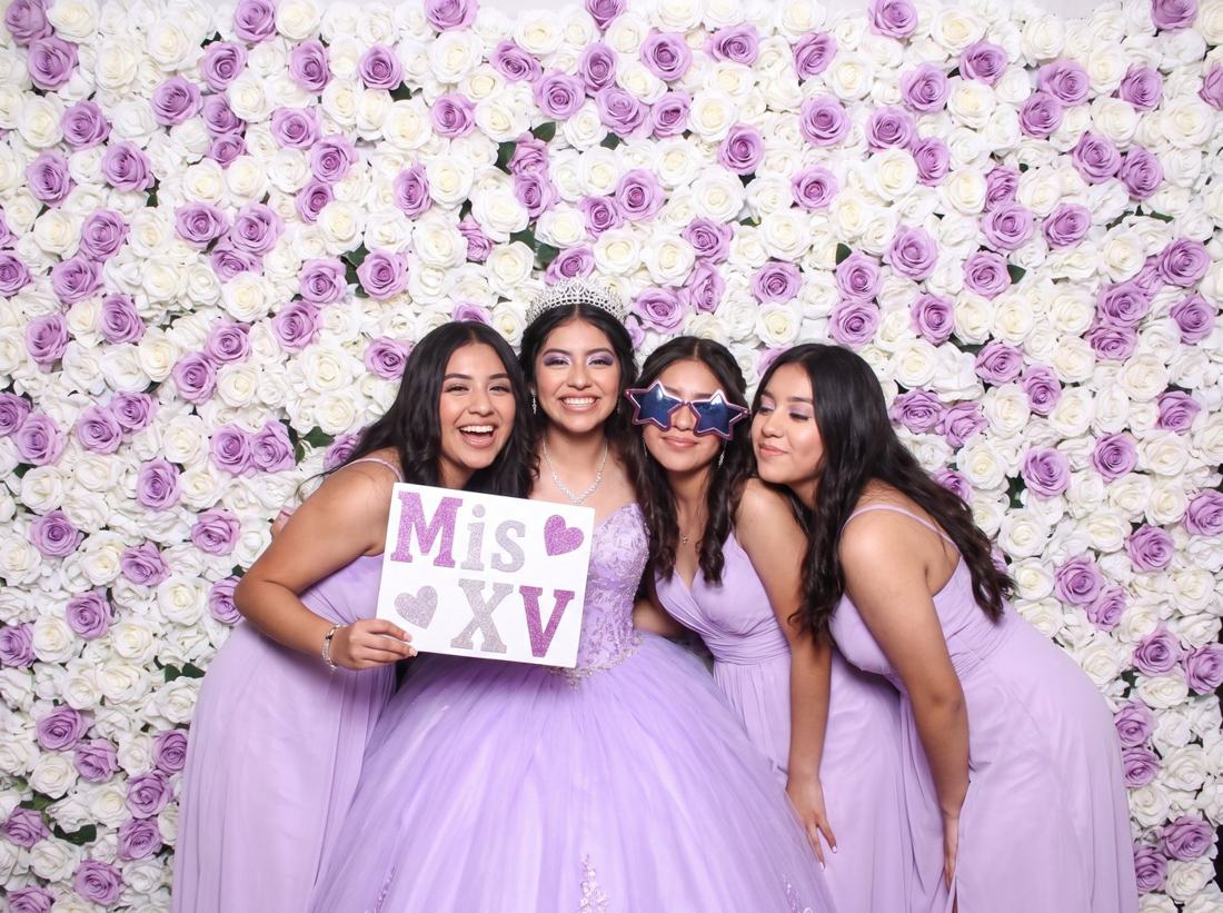 A quinceañera and her friends posing in front of a flower wall